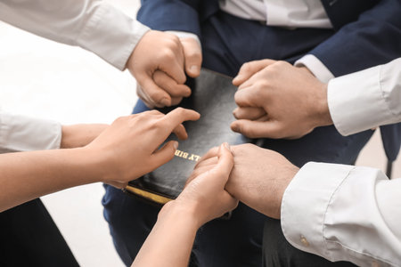 Group of people praying with Holy Bible in office, closeup