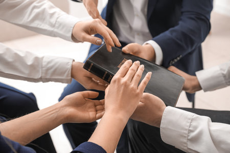 Group of people praying with Holy Bible in office, closeup
