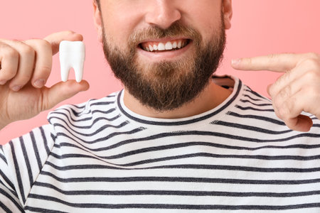 Young man with plastic tooth on color background, closeup