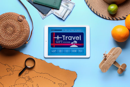 Tablet computer with gift voucher and travel accessories on color background