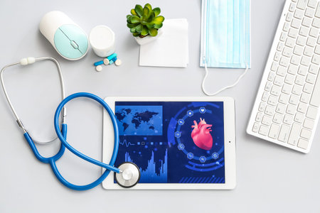 Tablet computer with stethoscope and accessories of doctor on gray background