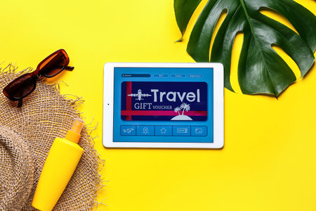 Tablet computer with gift voucher and travel accessories on color background