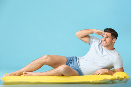 Young man lying on inflatable mattress against color backgroundの写真素材