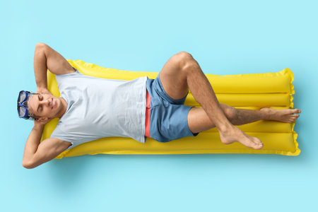 Young man lying on inflatable mattress against color backgroundの写真素材