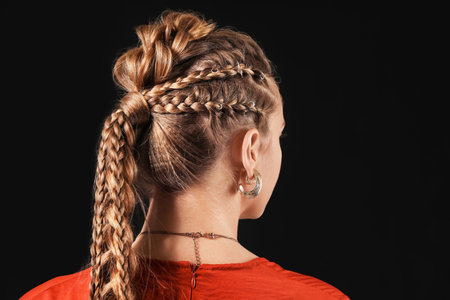 Beautiful young woman with braided hair on dark background