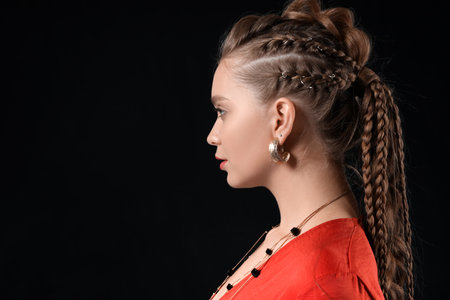 Beautiful young woman with braided hair on dark background