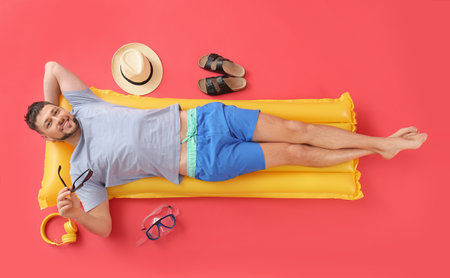 Handsome man lying on inflatable mattress against color background