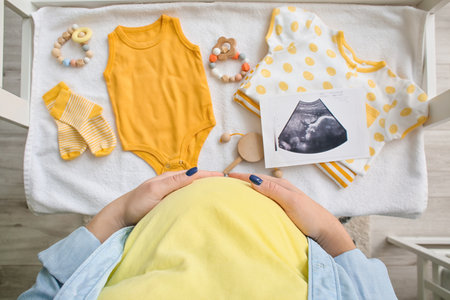 Pregnant woman near table with sonogram image, baby clothes and accessories
