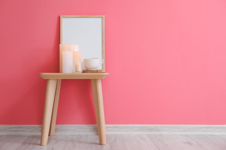 Burning candles and blank frame on table near color wallの写真素材