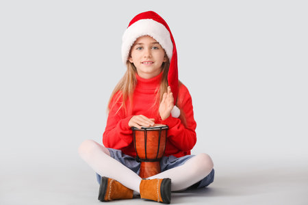 Cute little girl in Santa hat and with drum on light backgroundの写真素材
