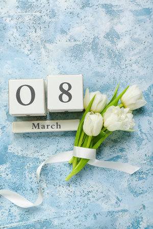 Cube calendar with date MARCH 8 and bouquet of beautiful tulip flowers on color background