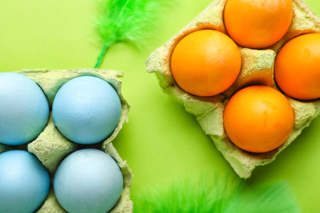 Cardboard holders with painted Easter eggs and feathers on green background, closeup