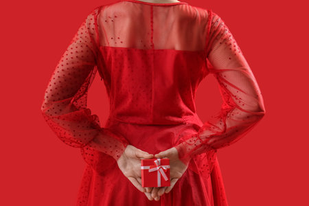 Woman in dress with gift box for Valentine's Day on red background, closeupの写真素材