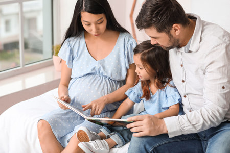 Pregnant Asian woman with her family reading book at homeの写真素材