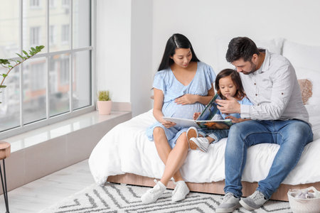 Pregnant Asian woman with her family reading book at homeの写真素材