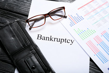 Wallet with document and paper sheet with word BANKRUPTCY on dark wooden background