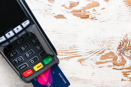 Payment terminal with credit card on light wooden background, closeup