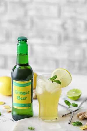 Bottle and glass of fresh ginger beer on light background