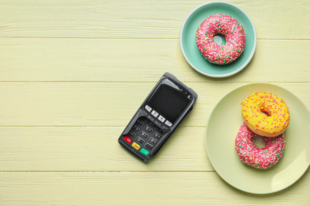 Payment terminal with donuts in plates on color wooden backgroundの写真素材