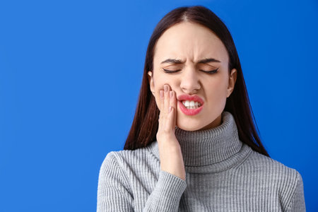 Young woman suffering from toothache on color backgroundの写真素材