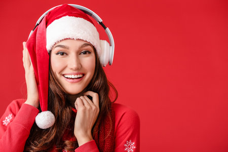 Beautiful young woman listening to Christmas music on color backgroundの写真素材