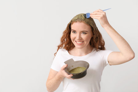 Young woman using henna hair dye on light backgroundの写真素材