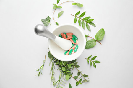 Mortar with pills and different herbs on white backgroundの写真素材