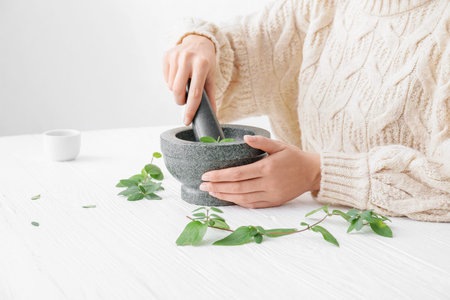 Woman grinding herbs in mortar on white wooden table