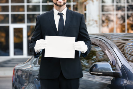 Handsome chauffeur with blank paper sheet near luxury carの写真素材