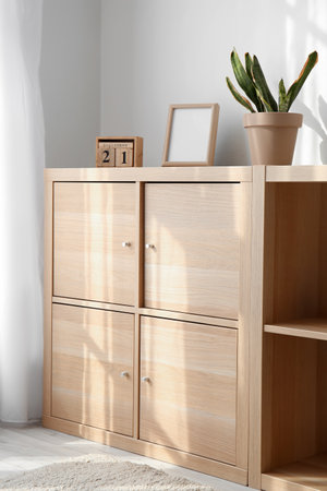 Wooden chest of drawers with calendar, frame and houseplant near light wallの写真素材