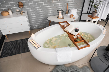 Stylish interior of modern bathroom with burning candles and glass of wine