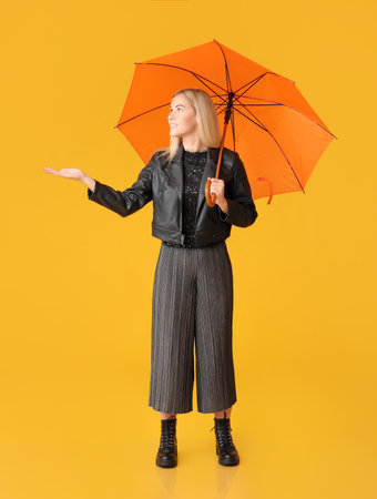 Stylish young woman with umbrella on color backgroundの写真素材