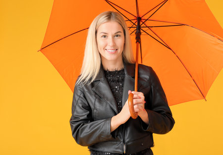 Stylish young woman with umbrella on color backgroundの写真素材