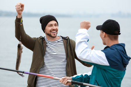 Happy father and son caught fish on river bankの写真素材