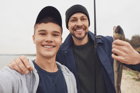 Happy father and son taking selfie while fishing on river, closeupの写真素材