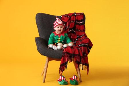 Cute little baby in elf's costume sitting in armchair against color backgroundの写真素材