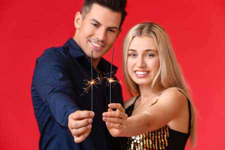 Happy young couple with Christmas sparklers on color backgroundの写真素材