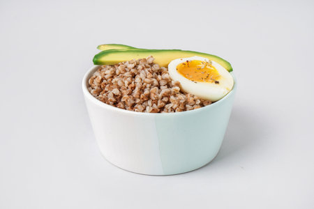 Bowl of tasty buckwheat porridge with soft boiled egg and fresh cucumber isolated on white backgroundの写真素材