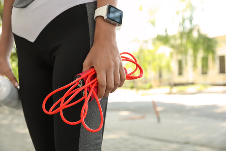 Sporty woman with skipping rope and bottle of water outdoors, closeupの写真素材