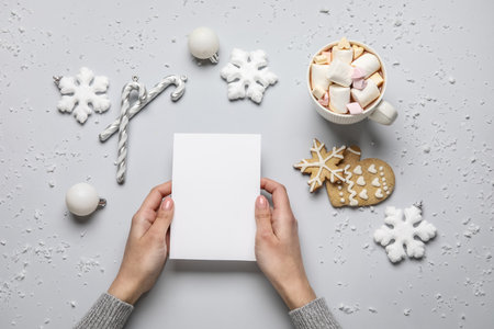 Woman holding paper sheet, cup of cocoa, cookies and Christmas decor on light backgroundの写真素材