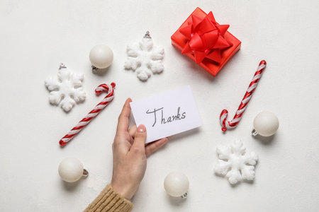 Woman holding paper sheet with word THANKS, gift and Christmas decor on white backgroundの写真素材