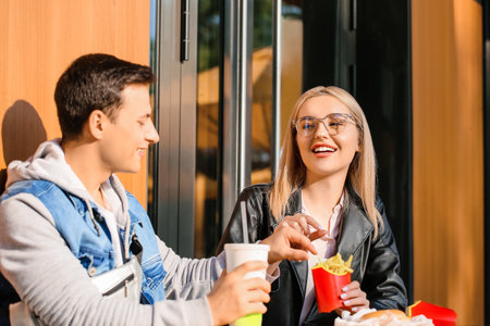 Young couple eating french fries in cafe outdoorsの写真素材