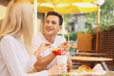 Young couple eating french fries in cafe outdoorsの写真素材