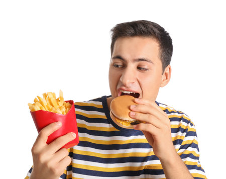 Young man with french fries eating burger on white backgroundの写真素材
