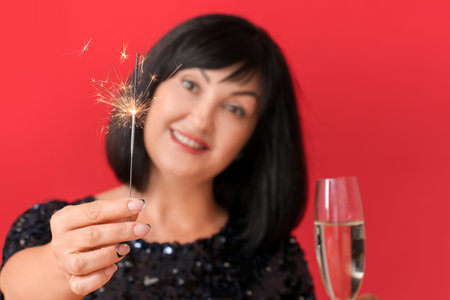 Mature woman with Christmas sparkler and champagne on color backgroundの写真素材