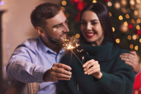 Young couple with sparklers celebrating Christmas at homeの写真素材