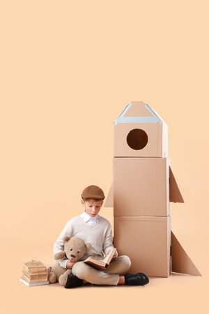 Cute little boy with books, toy and cardboard rocket on color backgroundの写真素材