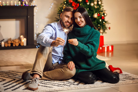 Young couple with sparklers celebrating Christmas at homeの写真素材