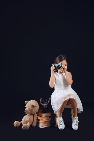 Cute little girl with books, photo camera and toy on dark backgroundの写真素材