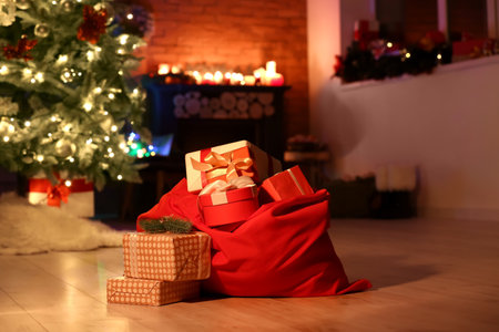 Santa bag with gifts and beautiful Christmas tree near fireplace in room at nightの写真素材